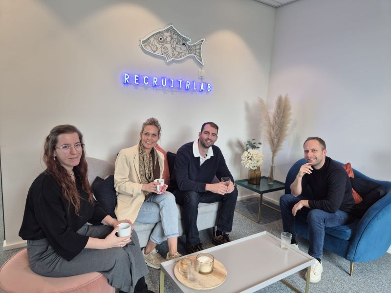 Het team van RecruitrLAB in de zithoek van het kantoor in Edegem, onder het neon vis-logo